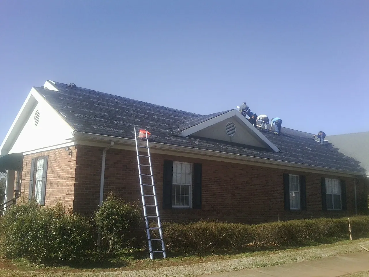 Crew tearing shingles off a brick ranch roof with a ladder set — Emergency Roof Repair work by our crew in Winfield